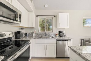 Een moderne keuken met witte kastjes, een granieten aanrecht, een ingebouwde oven, een vaatwasser en een raam met uitzicht op bomen.