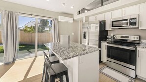Una cocina moderna con una isla central, electrodomésticos de acero inoxidable y un ventanal corredero hacia un patio trasero.