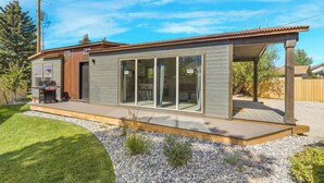Una casa moderna con un patio, una barbacoa y un amplio ventanal corredera.