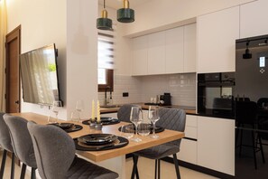 A modern kitchen with white cabinetry, a black refrigerator, and a dining area with a wooden table set for four. - Irisma Luxury Villa I | Private Pool near Heraklion, Crete (Archanes)
