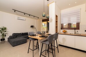 A modern living space with a dining area, a sofa, a kitchen, and a potted plant. - Irisma Luxury Villa I | Private Pool near Heraklion, Crete (Archanes)