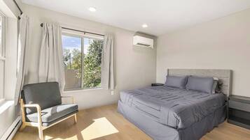 Ein Schlafzimmer mit einem Bett, einem Sessel, einem Fenster mit Vorhängen und einer Klimaanlage.