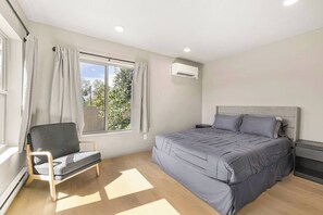 A bedroom with a bed, a chair, a window with curtains, and an air conditioning unit. - New Home! Teton Bungalow A - 1 Bedroom & LOFT! (Driggs)