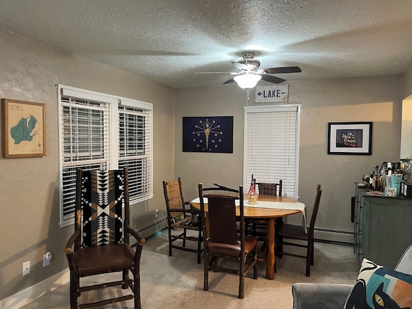 A dining area with a round table, chairs, a ceiling fan, and a wall-mounted sign indicating 'LAKE'.