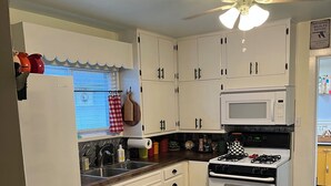 A kitchen with white cabinets, a microwave, an oven, and a ceiling fan.