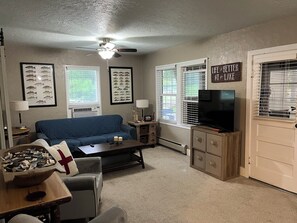 A living room with a blue sofa, a coffee table, a TV on a wooden stand, and framed fish pictures on the wall.