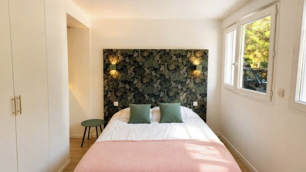 A bedroom with a bed, a headboard with wall-mounted lights, a small round table, and a window with a view of the outside. - EXCEPTIONAL VILLA IN SAINT-PALAIS-SUR-MER - HEATED POOL - 5 BEDROOMS (Saint-Palais-sur-Mer)