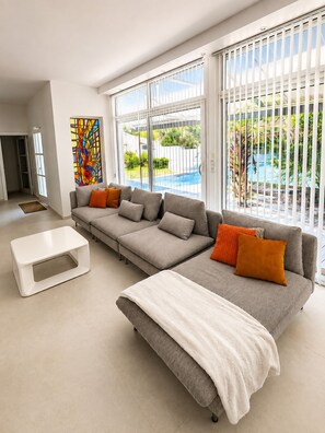 Ein modernes Wohnzimmer mit einer Eckcouch, einem Couchtisch und Blick auf einen Swimmingpool durch große Fenster.