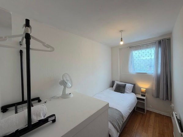 A bedroom with a bed, bedside table, lamp, and a standing fan.