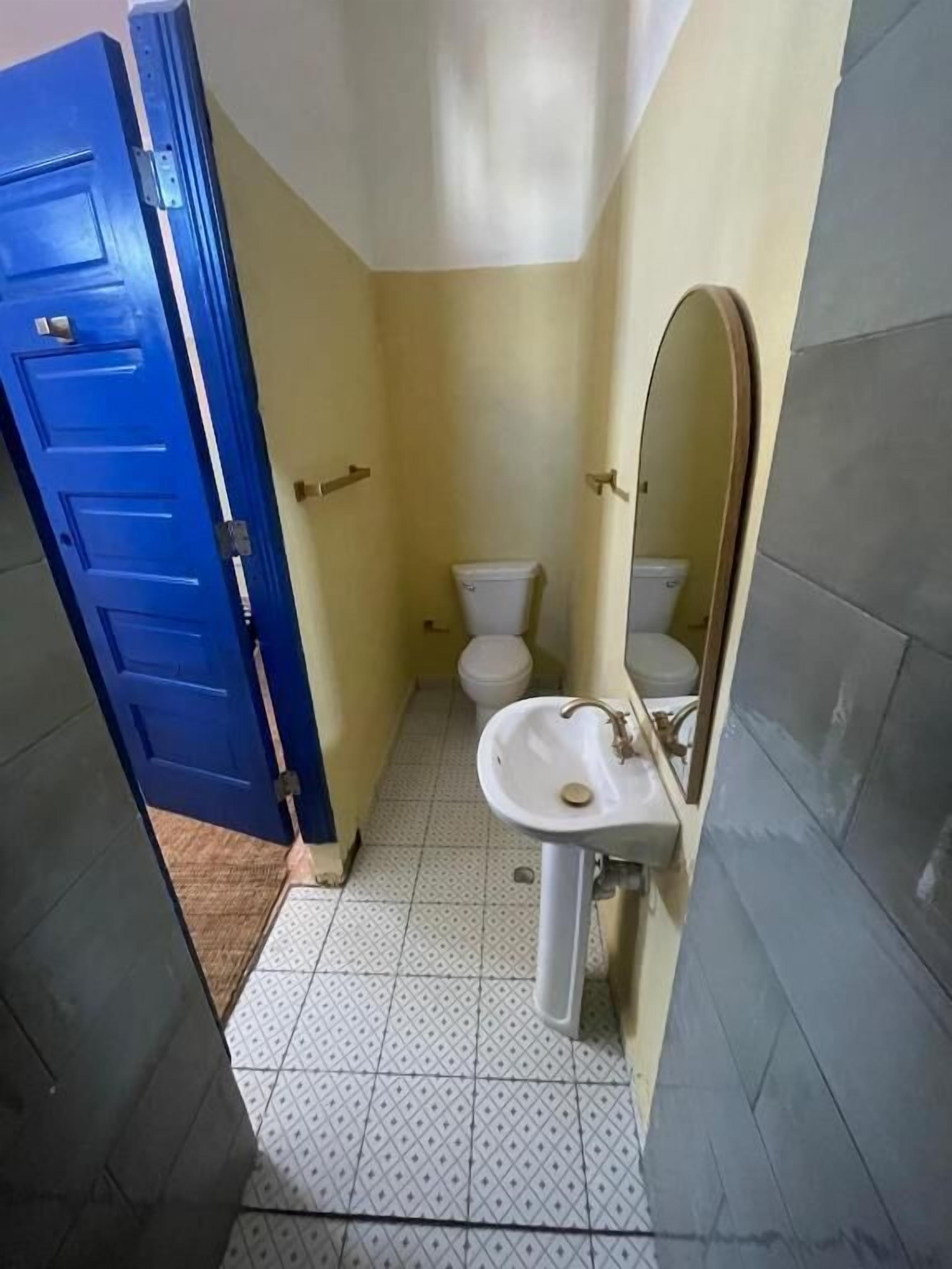 Um banheiro estreito com porta azul, pia branca e vaso sanitário.