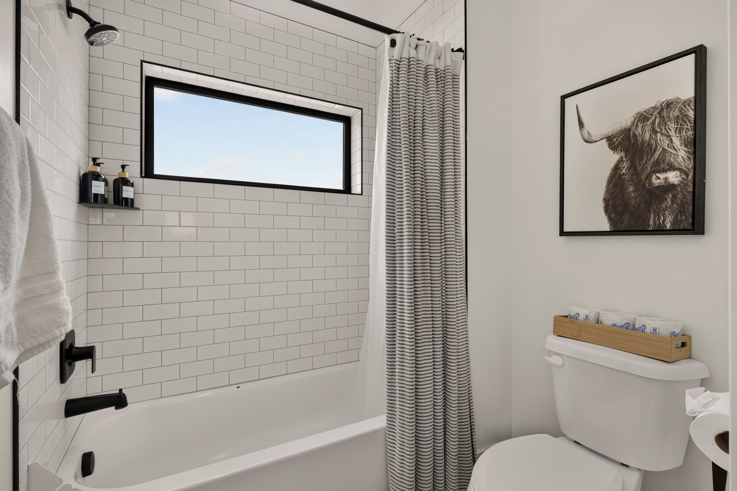 Une salle de bain avec une baignoire blanche, un rideau de douche, des toilettes et un tableau encadré au mur.