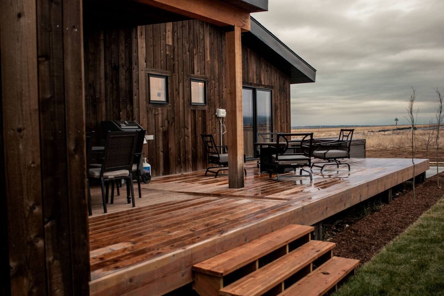 A wooden deck with outdoor furniture, a grill, and a view of the landscape.