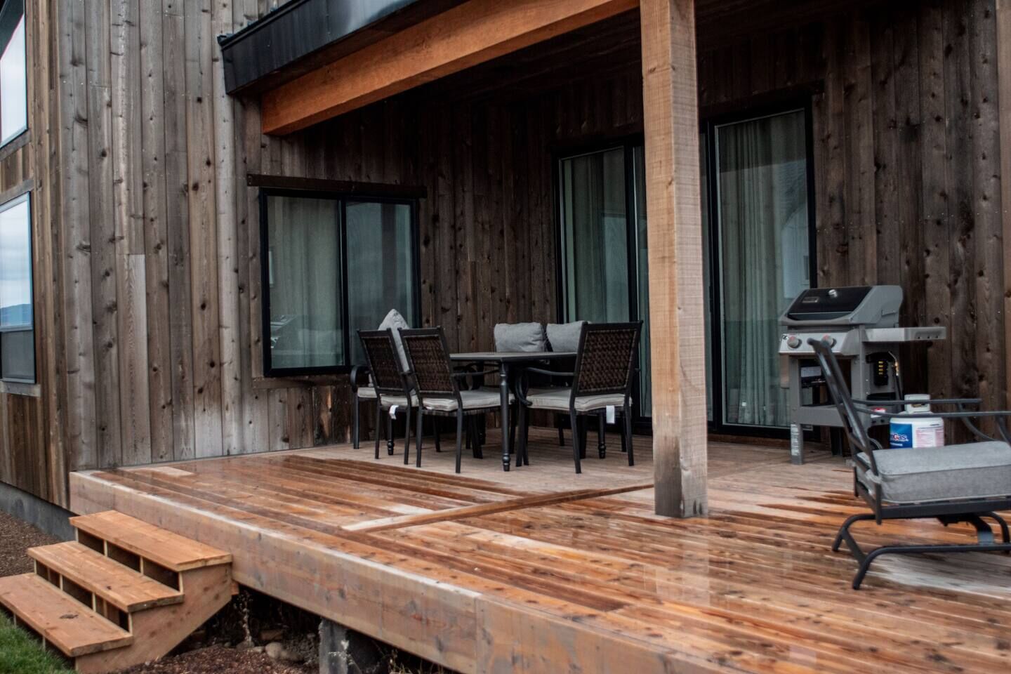 A wooden deck with outdoor furniture, a grill, and a staircase leading to an upper level.