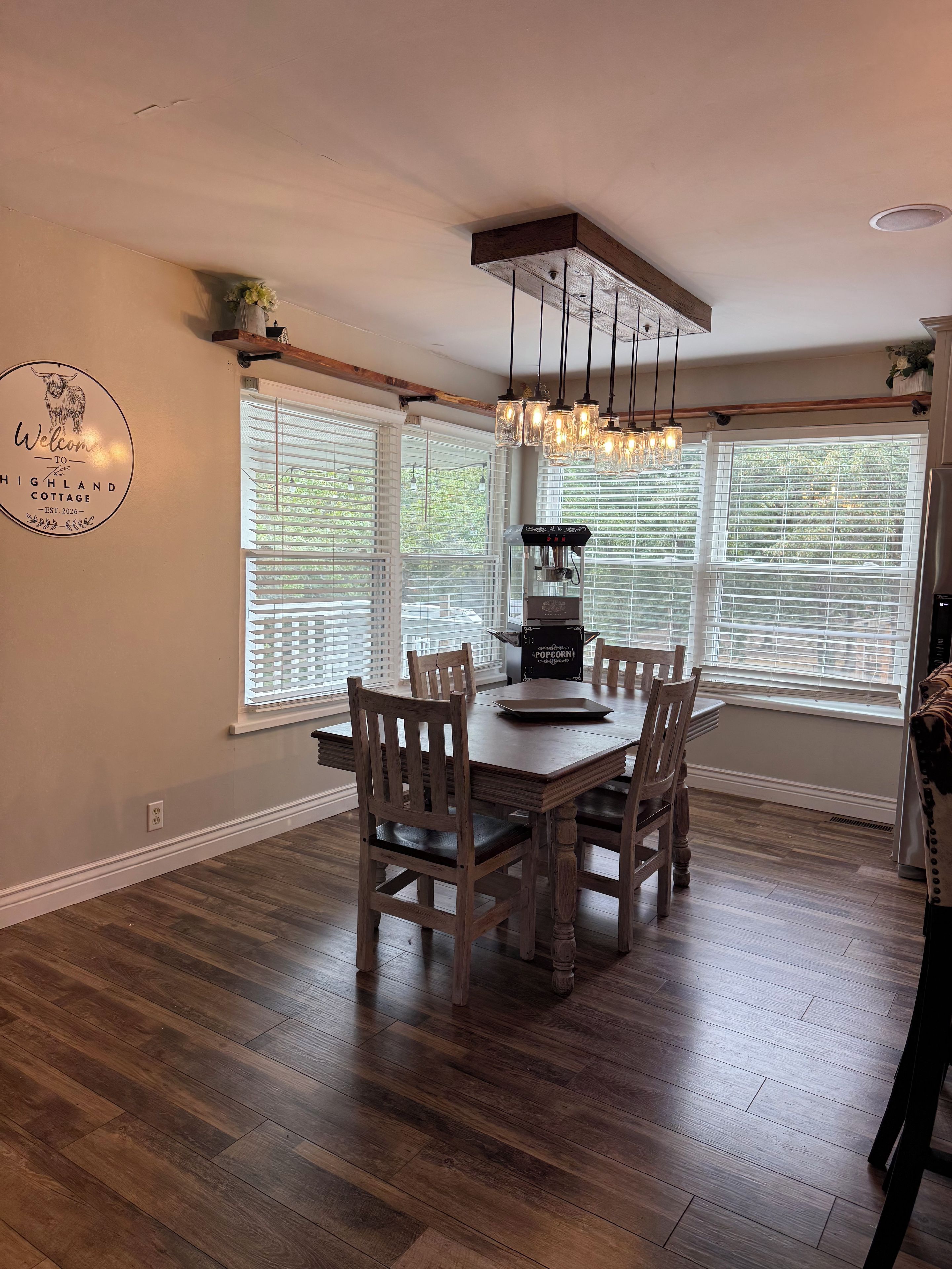 Un comedor con una mesa y sillas de madera, una cafetera y un letrero decorativo en la pared.