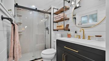 Une salle de bain moderne avec une douche à parois de verre, des toilettes blanches et un meuble-lavabo avec des accessoires dorés.