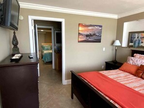A hotel room with a bed, a desk, a television, a painting, and a door leading to a bathroom. - 2BR/2BA Beach Condo- Full Kitchen-sleeps 4 (Daytona Beach)