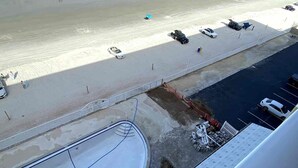 Ein Parkplatz neben einem Strand mit mehreren Autos und einigen Spaziergängern.