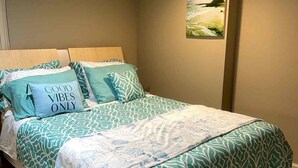 Ein Schlafzimmer mit einem Bett, Kissen, einem Gemälde an der Wand und einem Fliesenboden.
