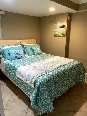 A bedroom with a bed, pillows, a painting on the wall, and a tiled floor. - 2BR/2BA Beach Condo- Full Kitchen-sleeps 4 (Daytona Beach)