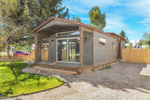Ein eingeschossiges Mobilheim mit überdachter Veranda, Glastür und Auffahrt mit Kies.