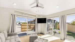 Uma sala de estar espaçosa com sofá, um banquinho e uma televisão de tela plana fixada na parede.