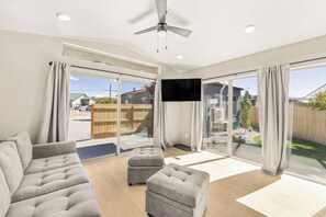 Ein geräumiges Wohnzimmer mit einer Couch, einem Hocker und einem an der Wand befestigten Flachbildfernseher.