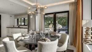 Uma sala de jantar com uma mesa redonda, cadeiras brancas e um candelabro.