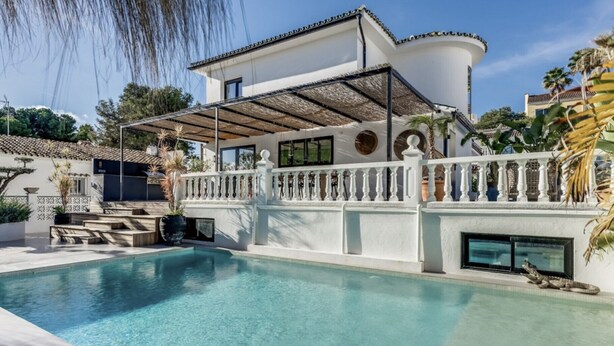 Uma villa moderna com piscina, alpendre coberto e cerca branca.
