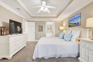Een slaapkamer met een bed, een dressoir, een televisie, een plafondventilator en kunst aan de muur.