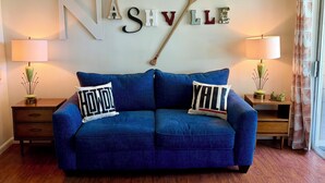 Ein blaues Sofa mit zwei Kissen, eine Wand mit dem Schriftzug 'NASHVILLE' und einem Schläger, sowie zwei Lampen auf Beistelltischen.