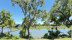 Blick auf einen See mit Bäumen und einer Rasenfläche.