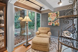 Une pièce avec une grande fenêtre, une chaise, une petite table et un élément décoratif mural.