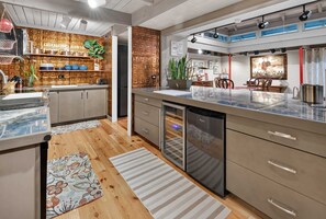 A modern kitchen with a wooden backsplash, stainless steel appliances, and a dining area with a marble countertop. - Artist's Cottage | Eclectic Retreat Near Coligny (Hilton Head Island)