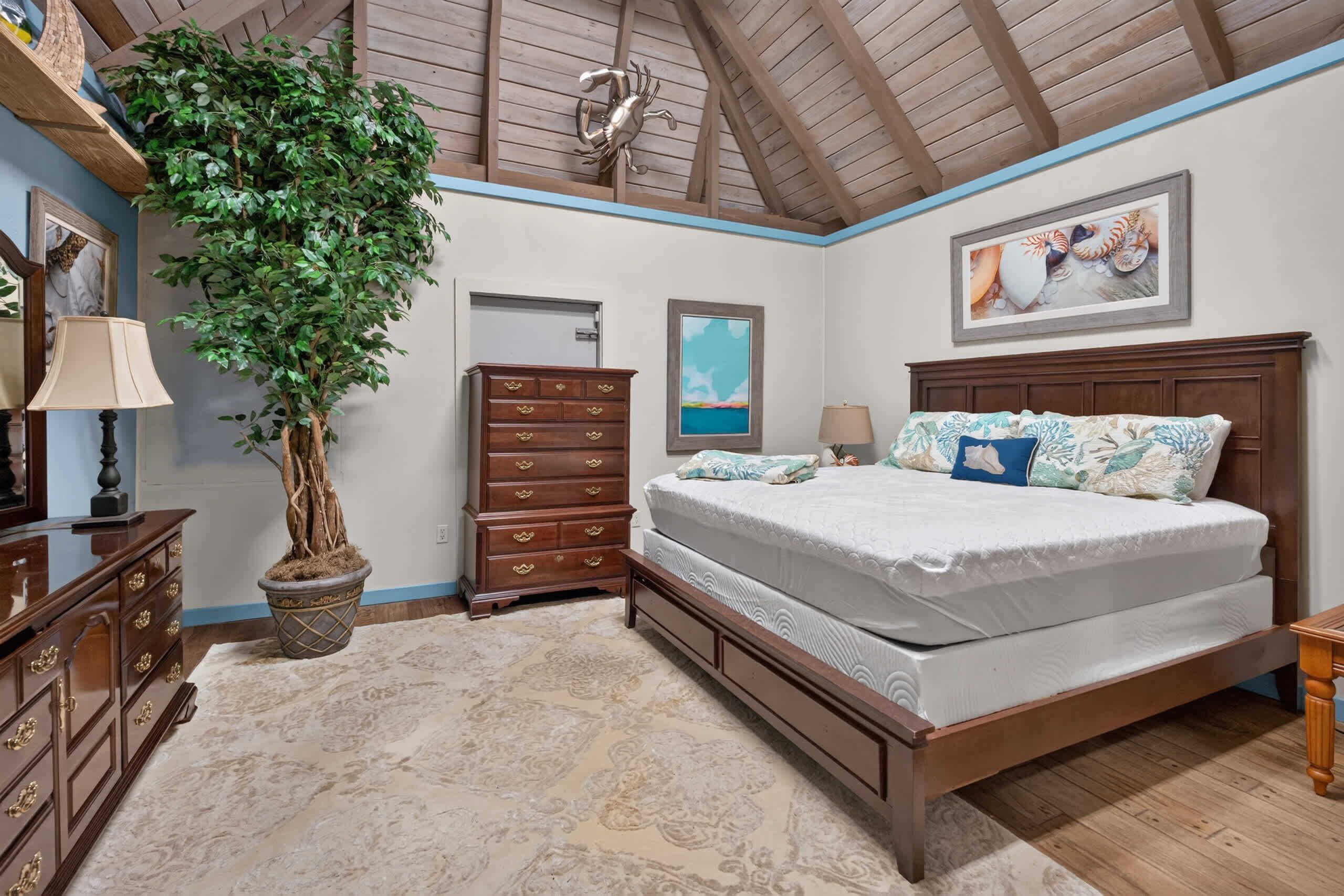 Une chambre à coucher avec un grand lit, une commode, un miroir, une plante en pot et un plafond avec des poutres en bois.