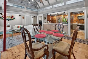 Ein geräumiger Essbereich mit Glastisch und Holzstühlen, eine Küche mit auffälliger, gemusterter Spritzschutzleiste und ein Wohnzimmer mit weißem Sofa und dekorativen Wandbildern.