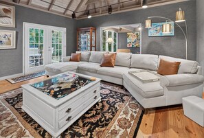 A modern living room with a sectional sofa, a glass coffee table with decorative items, a patterned rug, and artwork on the walls. - Artist's Cottage | Eclectic Retreat Near Coligny (Hilton Head Island)