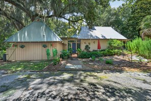 A two-story house with a covered porch and a small garden area. - Artist's Cottage | Eclectic Retreat Near Coligny (Hilton Head Island)