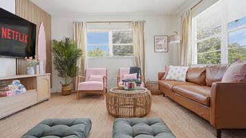 A living room with a television, two armchairs, a sofa, a coffee table, and a large window with curtains.