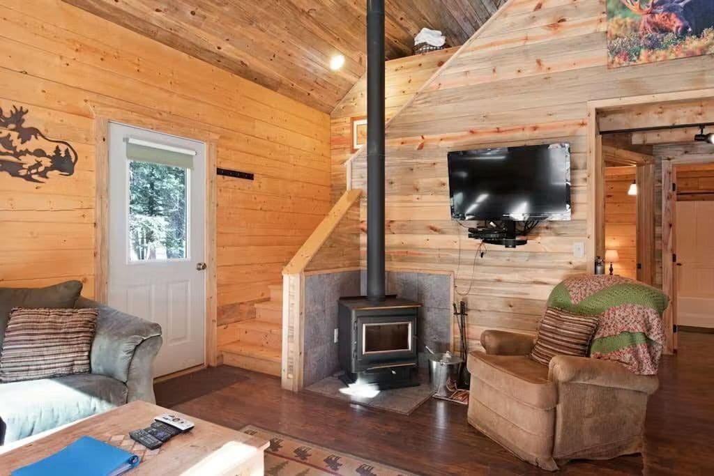 Ein gemütliches Blockhaus-Interieur mit Holzvertäfelung, Kamin, Wandfernseher und einer Couch.