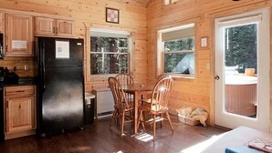 Ein Holzblockhaus-Interieur mit Essbereich, Küche und einer Tür, die nach draußen führt.