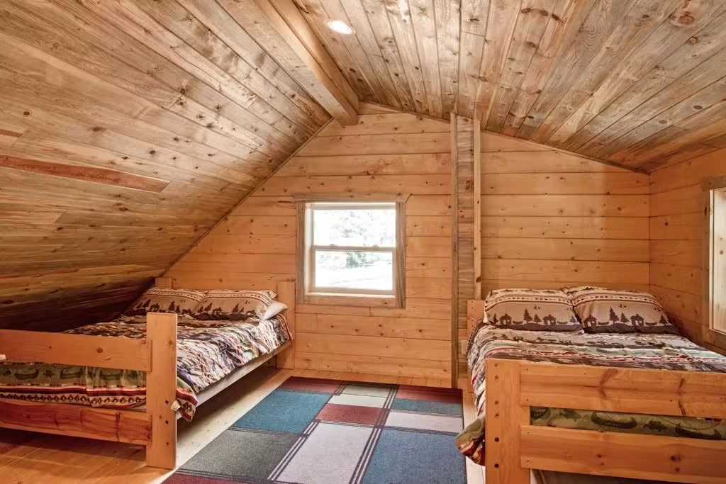 A cabin with two wooden beds, a window, and a sloped ceiling.