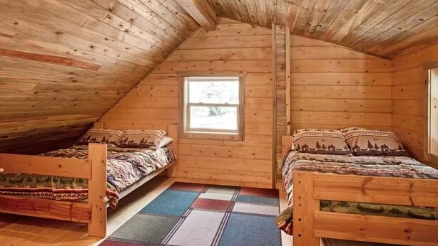 Eine Holzhütte mit zwei Betten, einem Fenster und einer geneigten Decke.