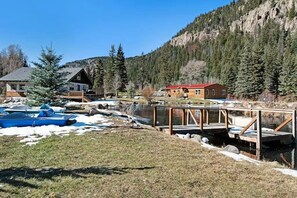 Eine Lodge mit einer Holzterrasse und einem kleinen Steg über dem Wasser, umgeben von bewaldeten Bergen.
