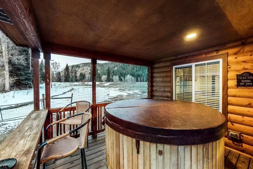 A wooden deck with a hot tub, chairs, and a view of a snowy landscape.