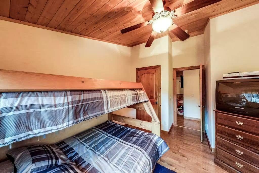 A bedroom with a bunk bed, wooden ceiling, and a television on a dresser.