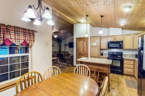 A wooden interior with a dining table, chairs, a kitchen area with cabinets and appliances, and a window with curtains. - Eldora Cabin | Hot Tub on the Rio Grande! (South Fork)