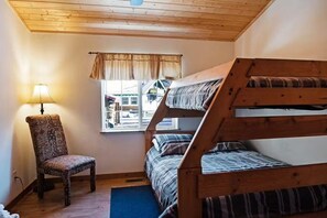 A room with a bunk bed, a chair, a lamp, and a window with a view of buildings outside. - Eldora Cabin | Hot Tub on the Rio Grande! (South Fork)