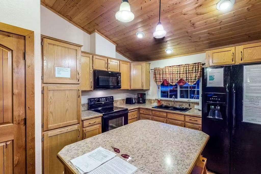 A kitchen with wooden cabinets, a granite countertop, a black refrigerator, and a microwave.