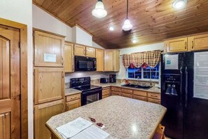 Eine Küche mit Holzausstattung, einer Granit-Arbeitsplatte, einem schwarzen Kühlschrank und einer Mikrowelle.
