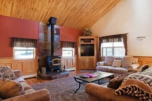 A cozy living room with a fireplace, wooden walls, a sofa set, and a television. - Gressoney Family Retreat | Pond & Hot Tub (South Fork)